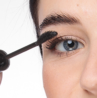 Una mujer se aplica rímel con una brocha, añadiendo volumen a sus pestañas y perfeccionando el maquillaje de sus ojos.