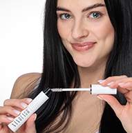 Una mujer sostiene elegantemente un tubo de rímel Nanolash, mostrando su belleza y confianza en un ambiente elegante.