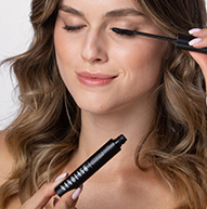 Una mujer se aplica cuidadosamente rímel para realzar sus pestañas, concentrándose intensamente en su rutina de maquillaje.