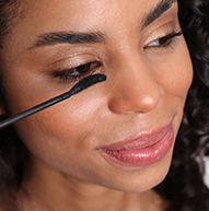 Una mujer se aplica rímel en el ojo, mostrando su proceso de aplicación de maquillaje en un ambiente luminoso y elegante.