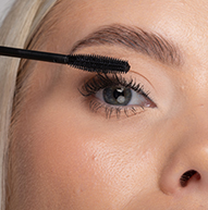 Una mujer se aplica cuidadosamente el rímel en las pestañas con un cepillo para rímel, realzando el maquillaje de sus ojos con precisión.