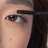 Se ve a una mujer aplicándose rímel con una brocha, centrándose en sus pestañas para lograr una mirada definida y elegante.